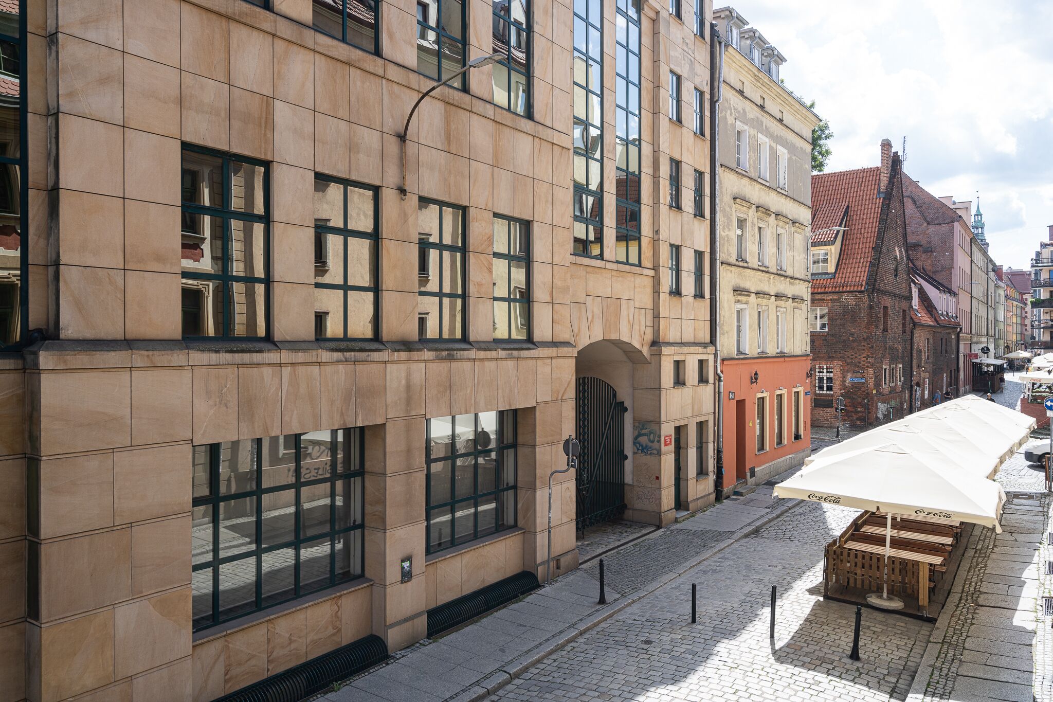 Un edificio con fachada de tejas, ventanas amplias y una zona de estar al aire libre con la marca Coca-Cola.