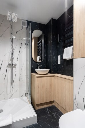 Un baño moderno con ducha envuelta en cristal, lavabo blanco y tocador de madera.
