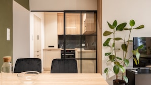 Una cocina moderna con encimera negra, armarios de madera y una puerta de cristal que da a un comedor con mesa y sillas de madera.