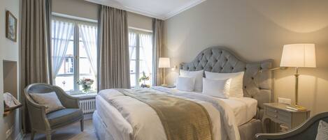 A hotel room with a large bed, two bedside tables, a chair, and a window with curtains.