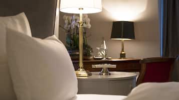 Una habitación de hotel con una cama, una mesita de noche con lámpara, un adorno y un florero con flores.