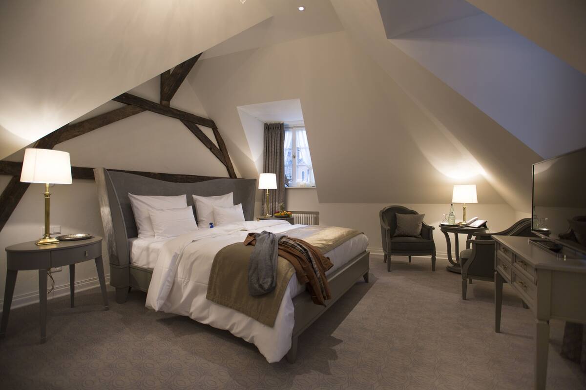 Une chambre à coucher avec un grand lit, deux tables de chevet, une chaise, un bureau et un miroir.