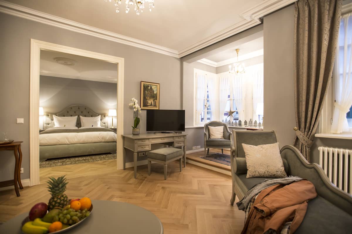 Une pièce bien éclairée, avec un lit, un bureau doté d’une télévision, un canapé et un panier de fruits.