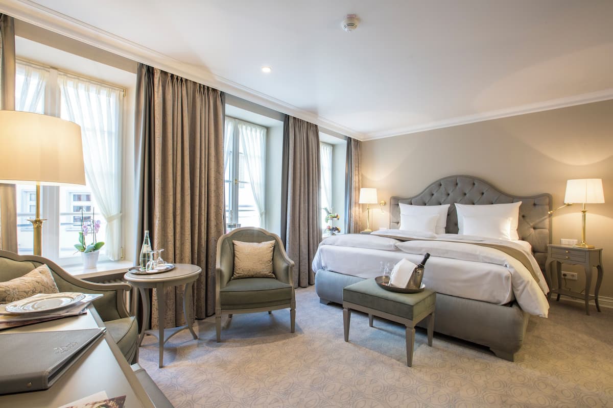 Une chambre d’hôtel avec un grand lit, un coin salon comprenant une chaise et une table, ainsi qu’une petite table d’appoint avec une lampe.