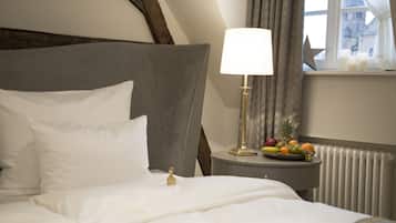 A hotel room with a neatly made bed, a bedside table with a lamp, and a fruit bowl on the windowsill.