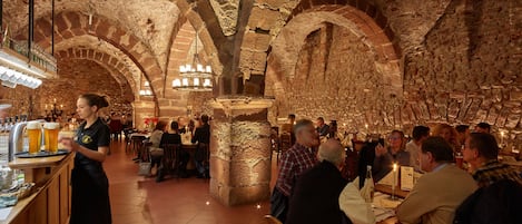 Un restaurante con paredes y arcos de piedra, mesas de madera y una zona de bar.