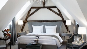 Een ruime, goed verlichte slaapkamer met een groot bed, twee nachtkastjes met lampen, een kroonluchter en uitzicht op de lucht via een dakraam.