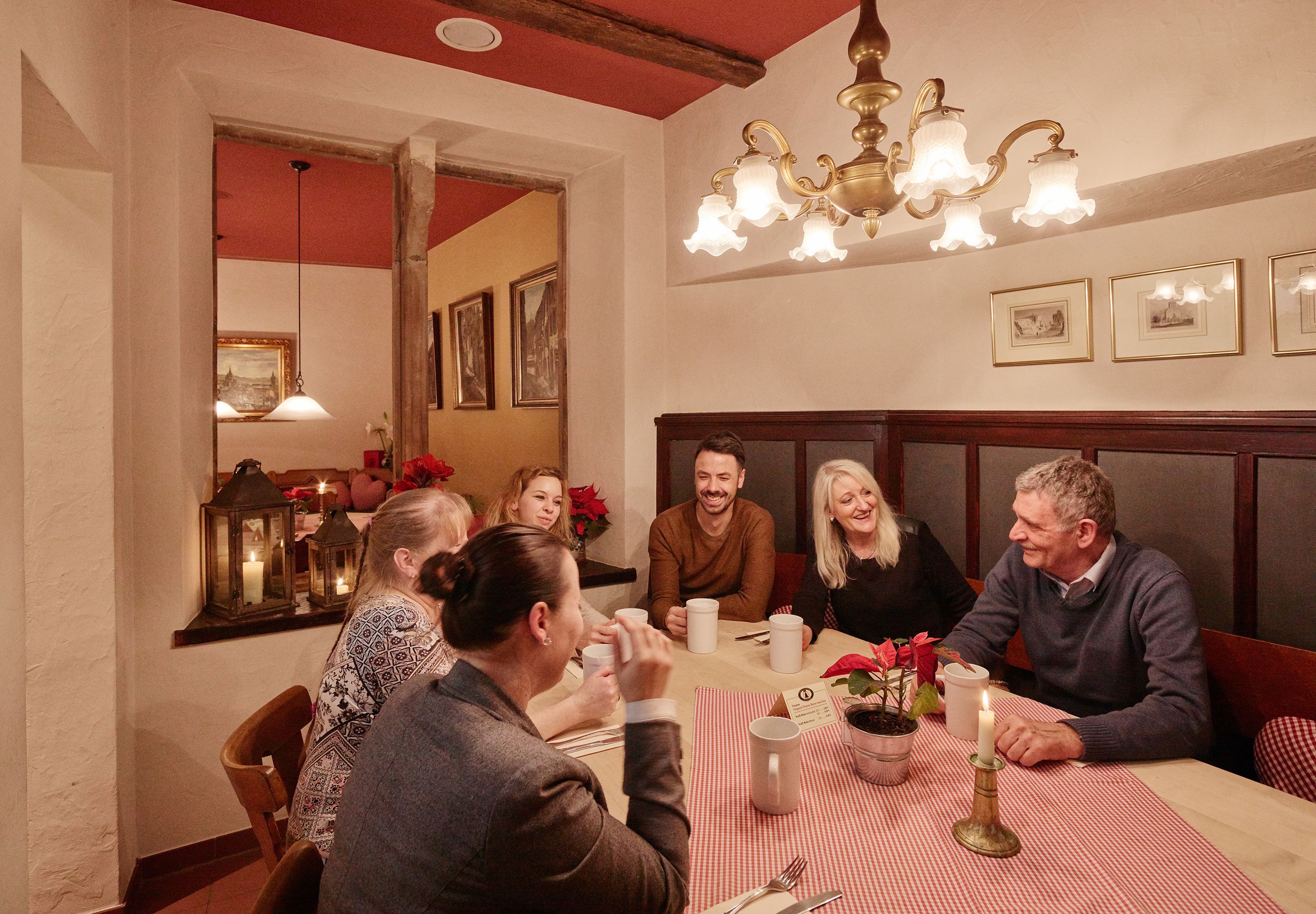 A group of people seated around a table with a checkered tablecloth, engaged in conversation.