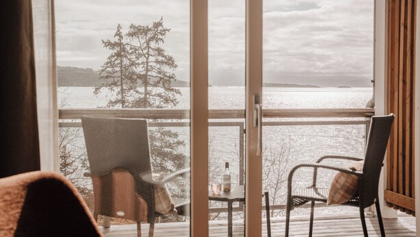 Une pièce avec vue sur un lac, deux chaises et une bouteille posée sur une petite table.