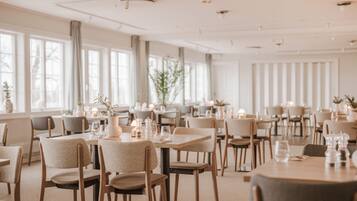 A spacious dining area with multiple tables and chairs, large windows, and a neutral color palette.