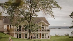 Un bâtiment à deux étages doté d’un balcon donnant sur un lac, le tout entouré de verdure.