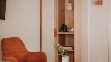 Una sala moderna con un sillón rojo, un jarrón blanco con una planta y una estantería de madera con varios objetos.
