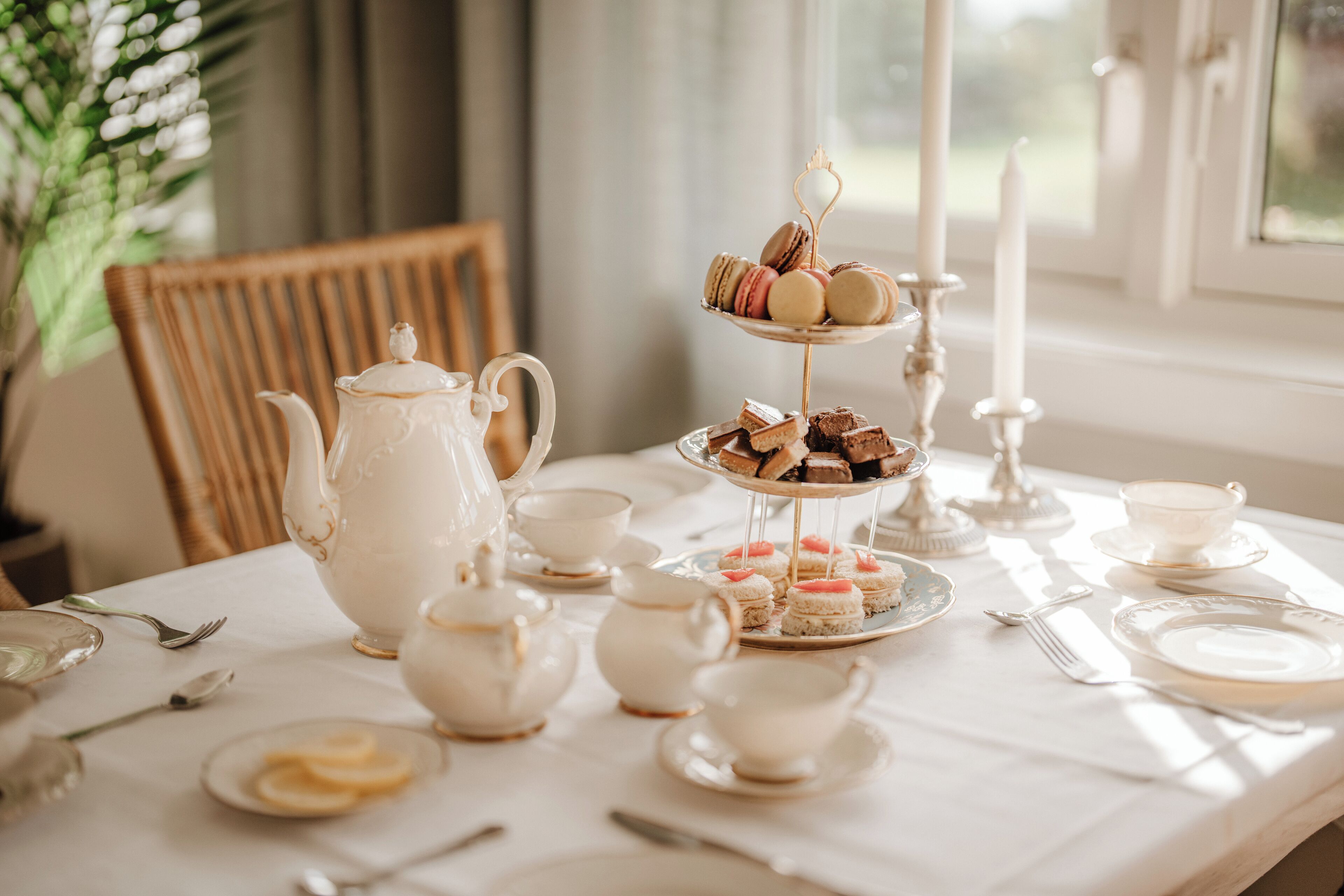 A tea setting with a tiered tray of pastries, a teapot, cups, and saucers on a table.