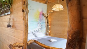A wooden cabin room with a bed, a tree branch decoration, and a wall painting. - Driftwood Villa (Kefalonia)