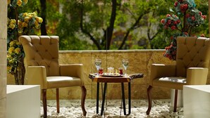 A sunlit outdoor seating area with two cushioned chairs and a small table, surrounded by white pebbles and featuring a view of trees and buildings. - Alba Ankara Hotel (Ankara)