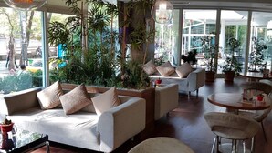A modern lounge area with a sofa, armchairs, and a round table. There are potted plants and a large window providing a view of the outdoors. - Alba Ankara Hotel (Ankara)