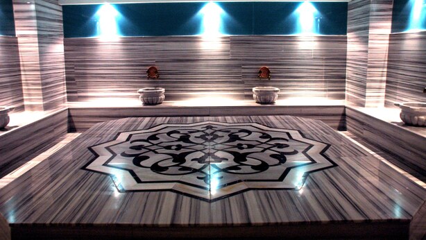 A bathroom with a large, ornate floor design, two sinks with faucets, and wall-mounted lighting. - Alba Ankara Hotel (Ankara)