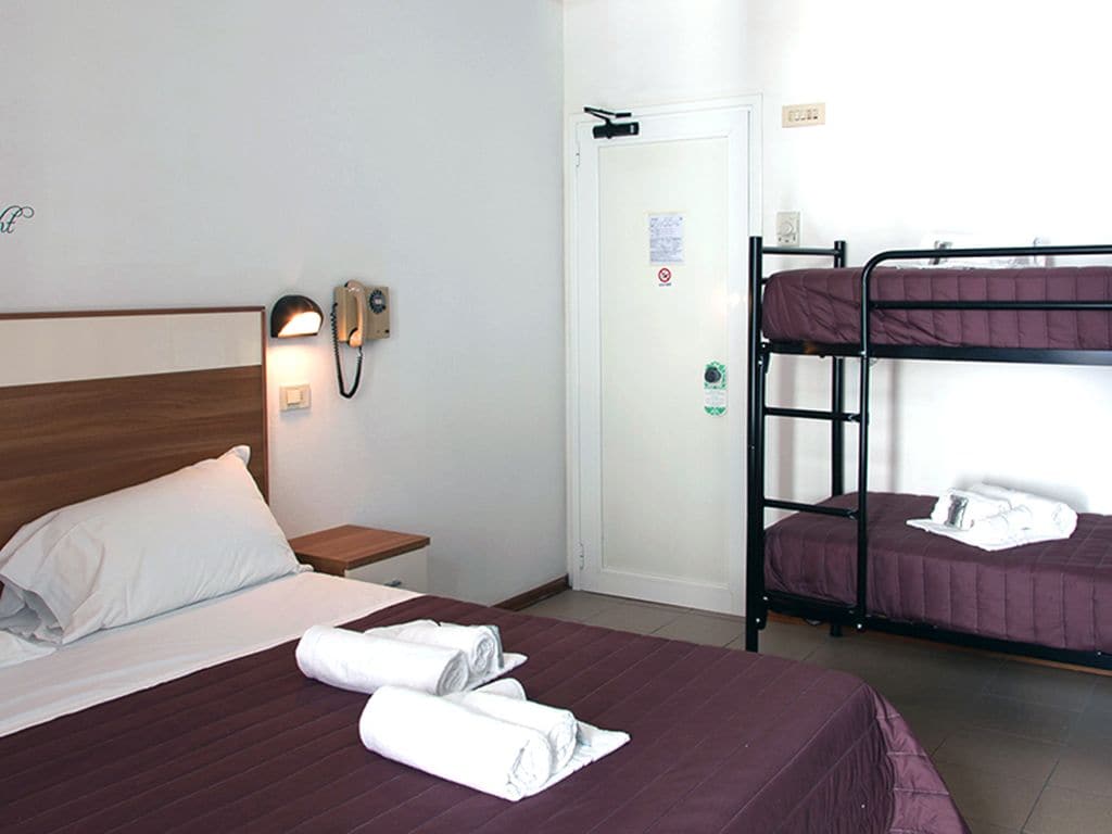 A hotel room with a single bed, a bedside table with a lamp, a phone, and a bunk bed with two beds.