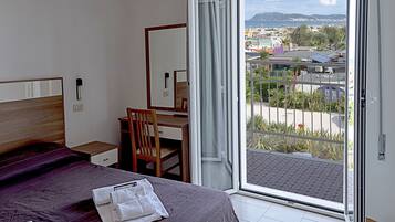 A hotel room with a bed, a desk, a chair, and a large window with a view of the city and mountains.