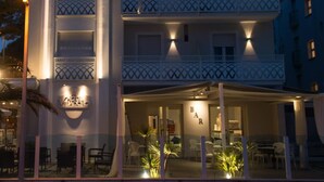 Een hotel met meerdere verdiepingen, balkons, buitenzitplaatsen en een goed verlichte entree.