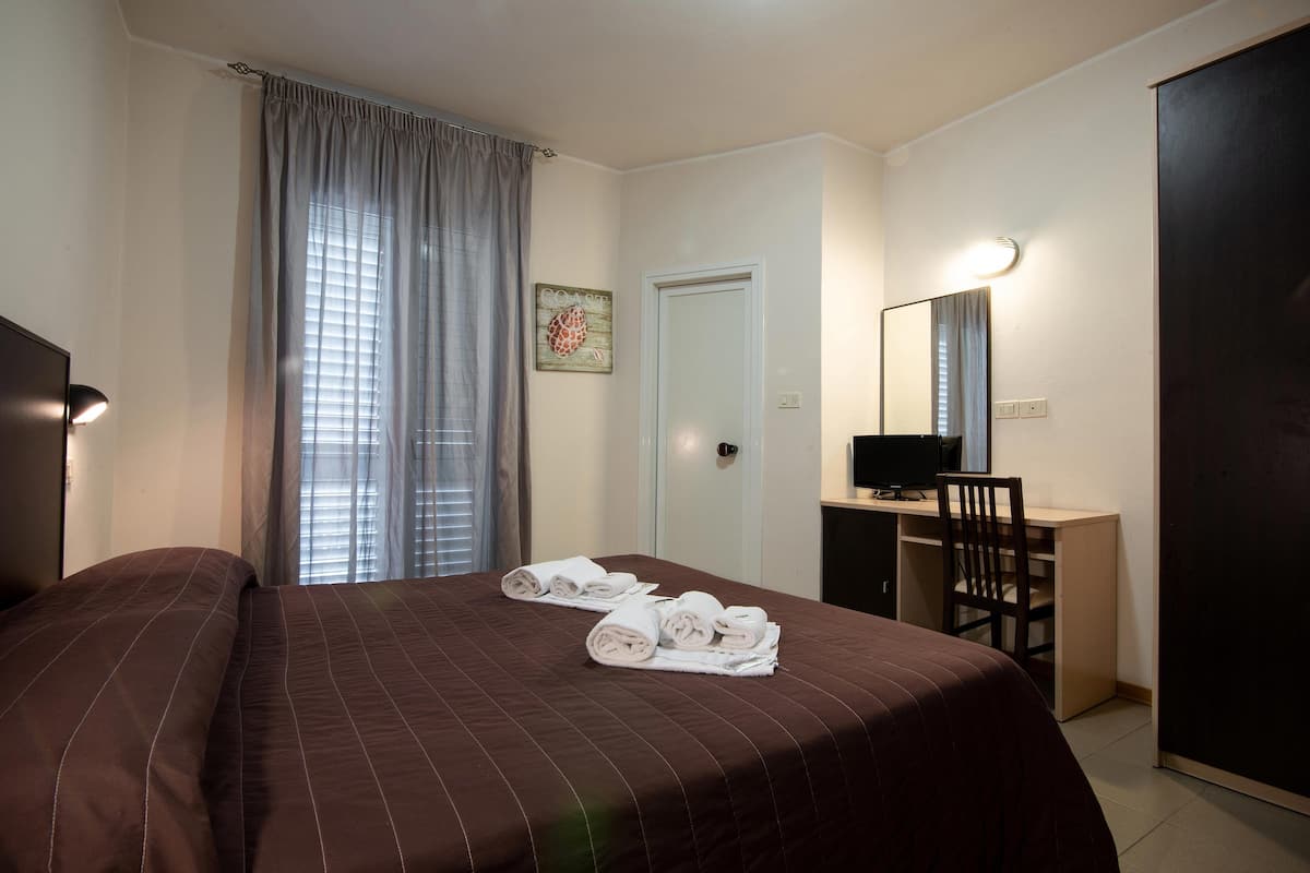 A hotel room with a bed, a desk, a chair, a TV, and a door.