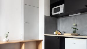 Une cuisine compacte équipée d’un four à micro-ondes, d’un petit réfrigérateur et d’une étagère en bois.