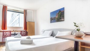 Une chambre d’hôtel avec deux lits, un bureau, des chaises, un vase avec des fleurs et un tableau au mur.