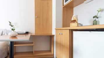 A compact kitchenette with a wooden cabinet, a white refrigerator, and a small table with a vase and a bowl.