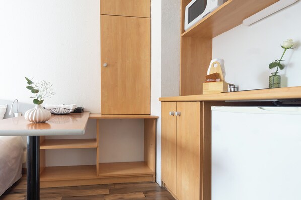 A compact kitchenette with a wooden cabinet, a white refrigerator, and a small table with a vase and a bowl.