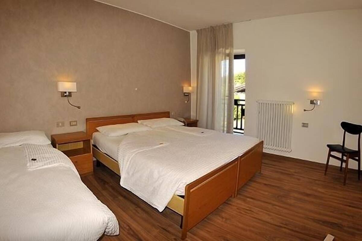 A hotel room with two single beds, wooden flooring, a radiator, and a chair.