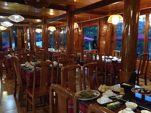 A restaurant with wooden interiors, tables set with dishes, and large windows. - Sapa Garden Resort (Sa Pa)