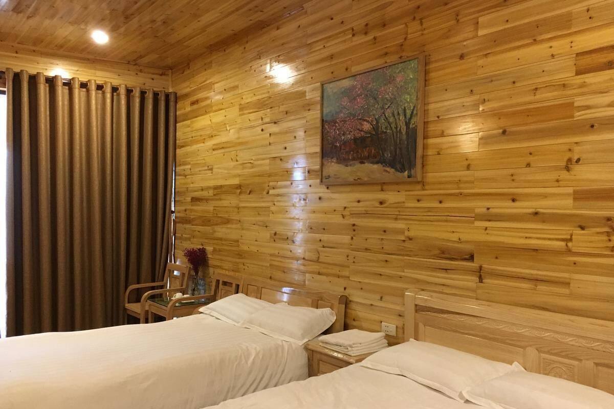 A wooden cabin room with two beds, a painting on the wall, and a chair with a vase of flowers.
