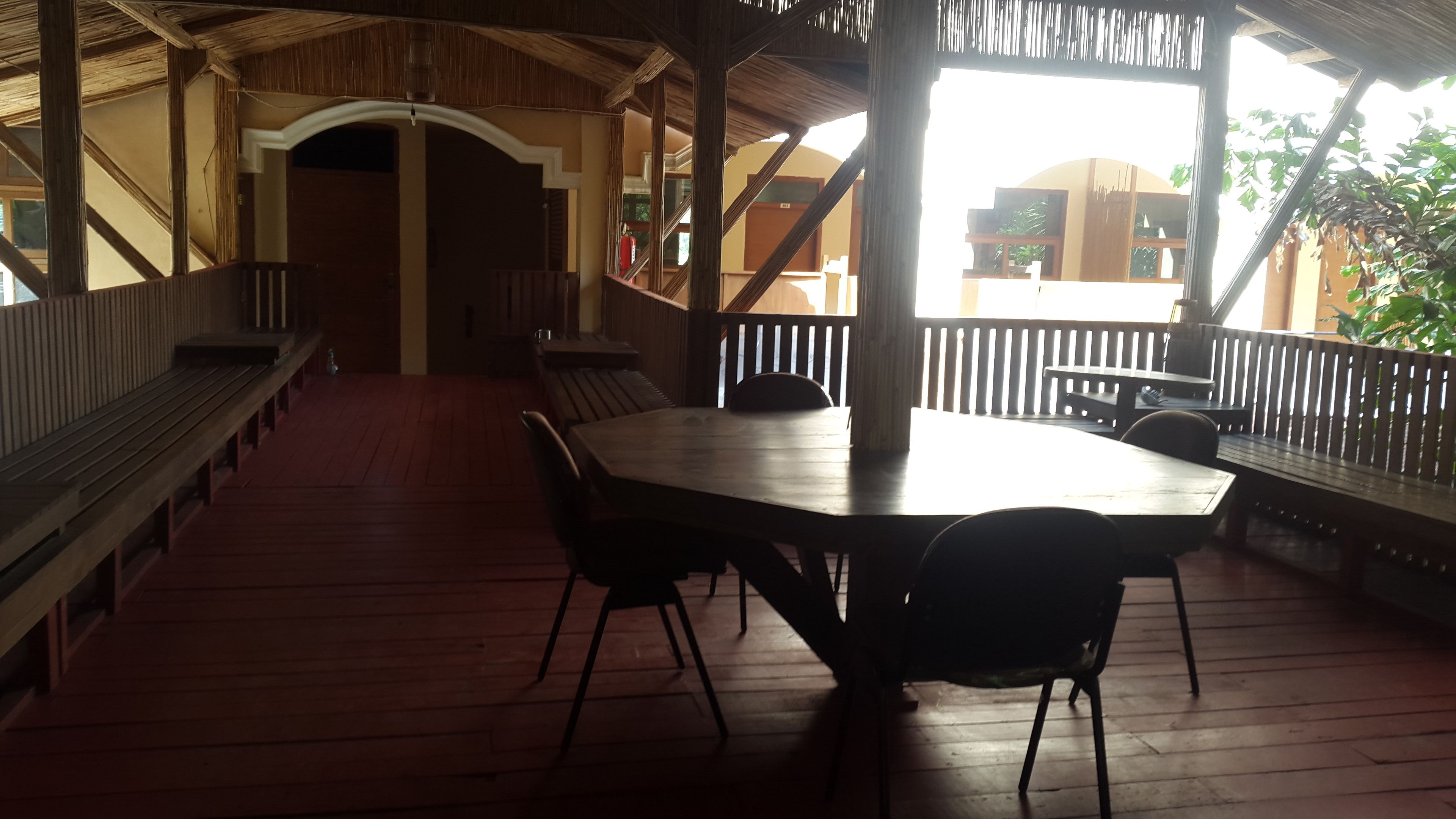 Un espace extérieur abrité avec une table et des bancs en bois, un escalier menant à un niveau supérieur et une vue sur les environs.