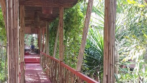 Eine Holzbrücke mit roter Oberfläche, gestützt von Bambuspfählen, umgeben von üppigem Grün.