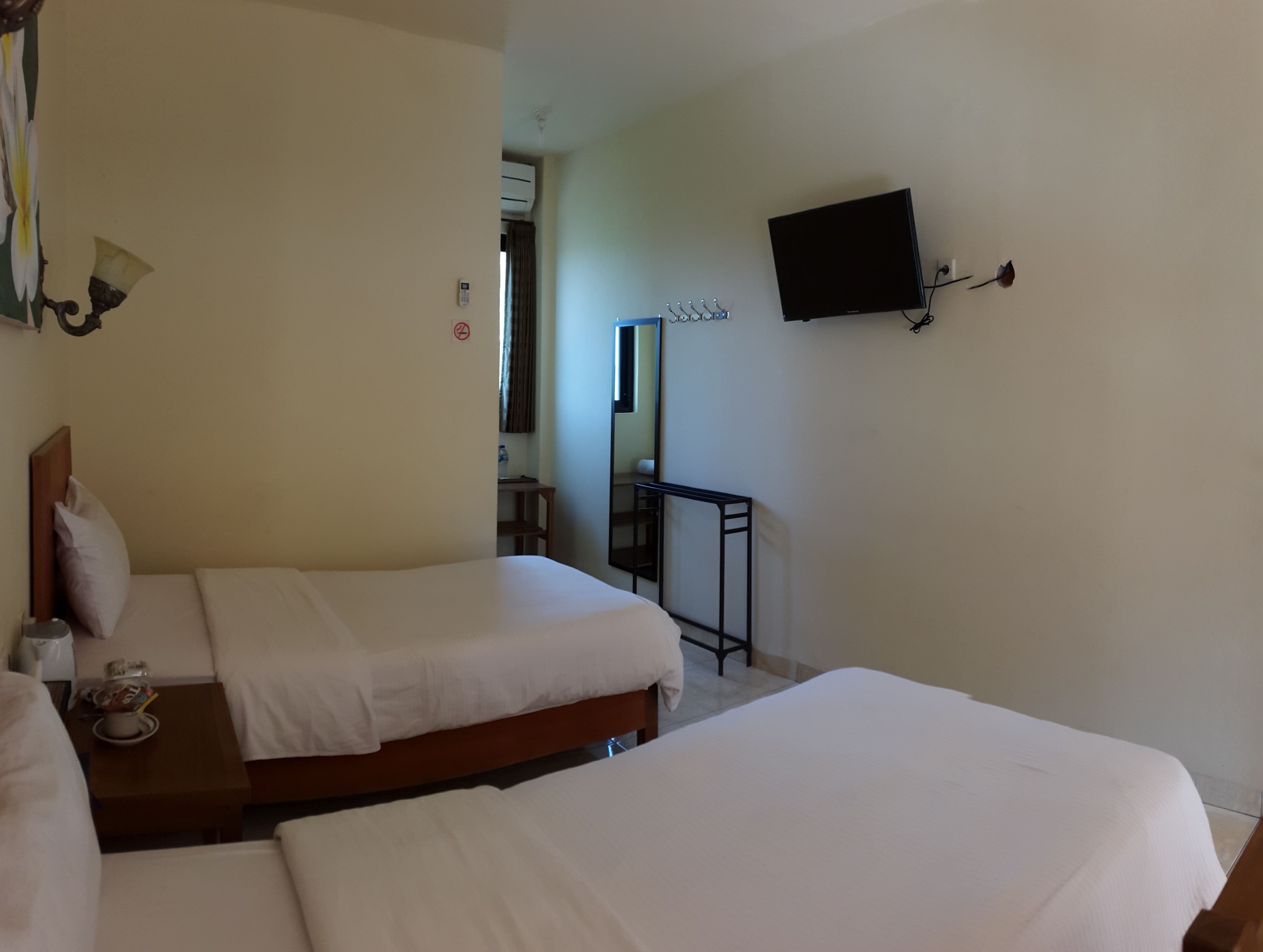 A hotel room with two beds, a flat-screen TV mounted on the wall, a small table with a bottle, and a mirror.