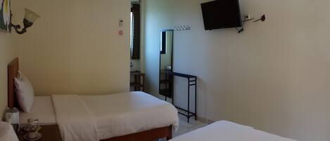A hotel room with two beds, a flat-screen TV mounted on the wall, a small table with a bottle, and a mirror.