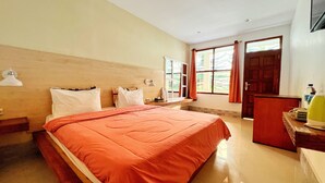 Ein Hotelzimmer mit Bett, Schreibtisch, Stuhl, einem Fenster mit Vorhängen und einer Tür.