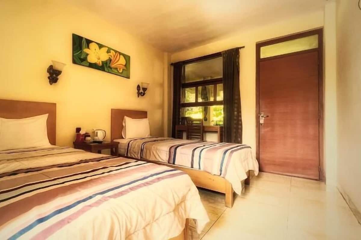 A room with two beds, a painting on the wall, a window with curtains, and a door.