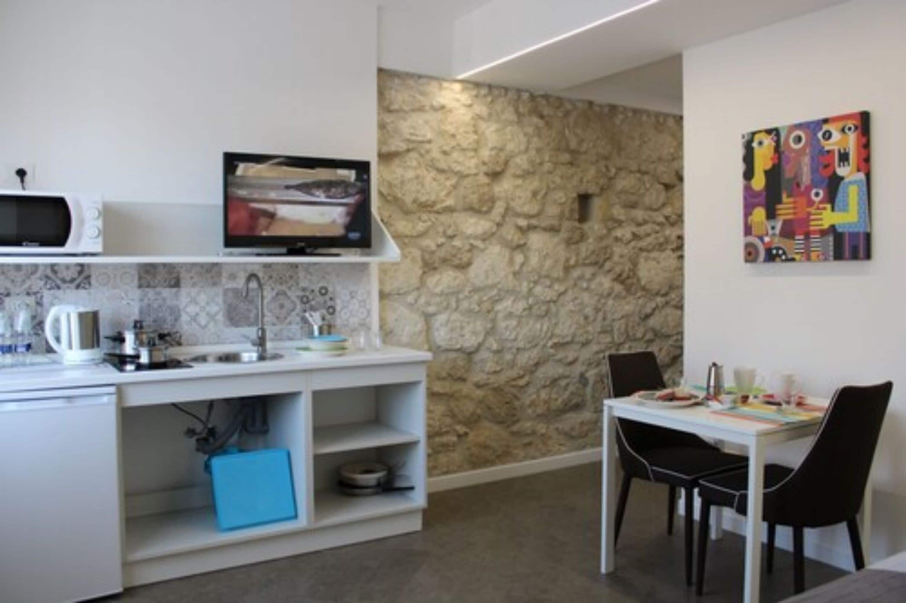 Une cuisine compacte avec un mur en pierre, un four à micro-ondes, une télévision et un coin repas comprenant des chaises et une table.