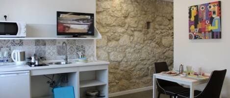 A compact kitchen with a stone wall, a microwave, a television, and a dining area with chairs and a table.