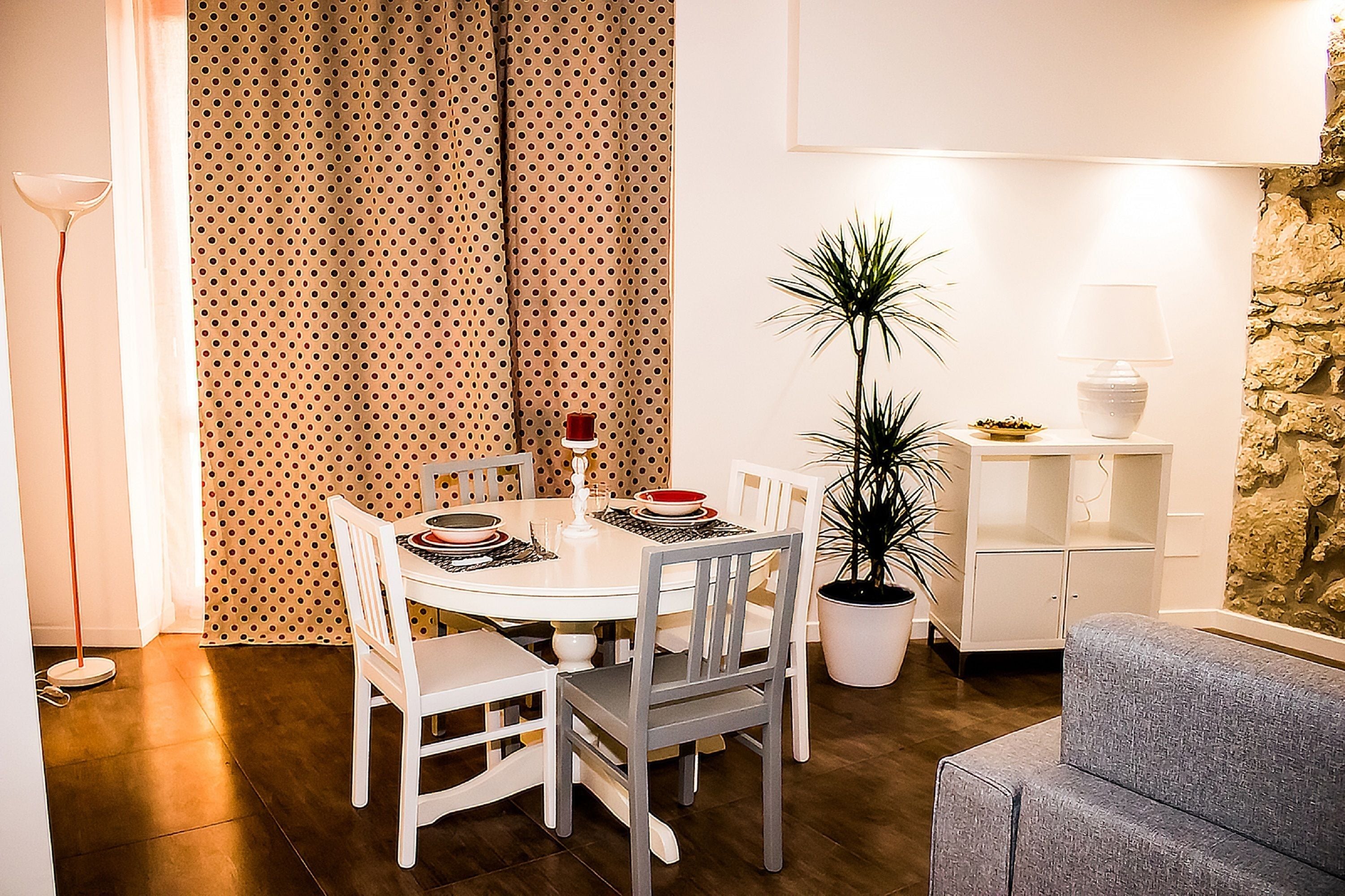 A dining area with a round table, white chairs, a potted plant, and a stone wall.