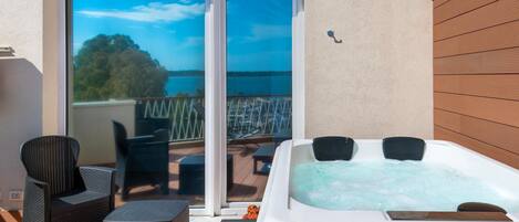 A hot tub on a balcony with a view of the sea, wicker furniture, and a sliding glass door.