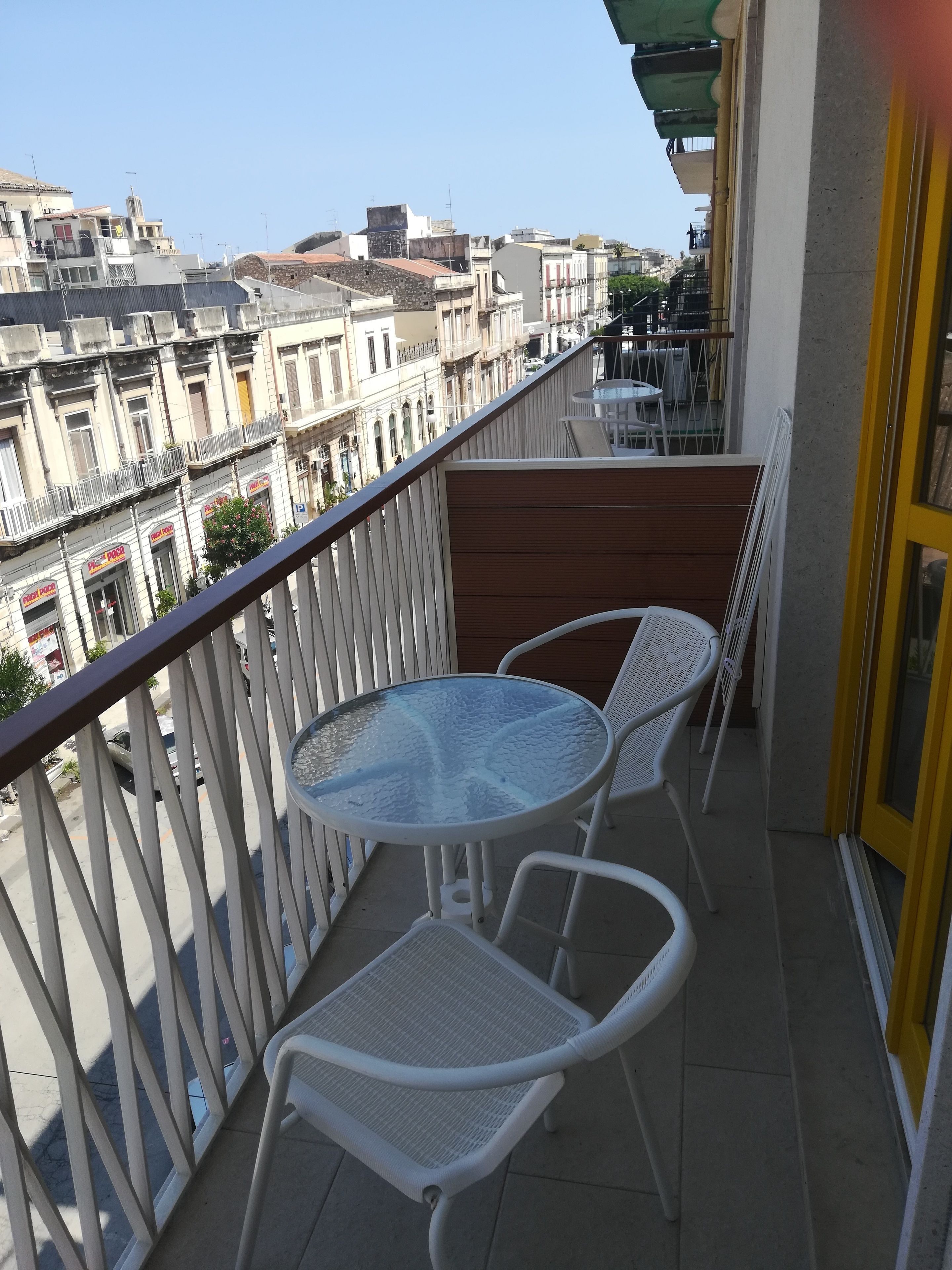 A balcony with a round table and two chairs, overlooking a cityscape with buildings and a street.