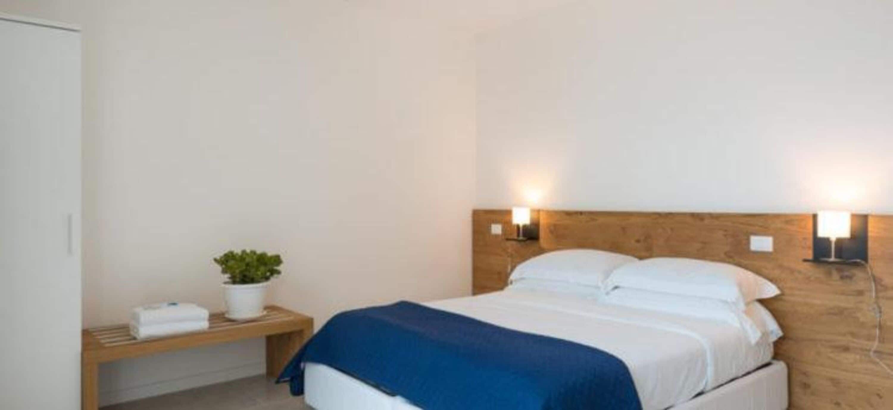 Un dormitorio con cama, mesita de noche e iluminación en la pared.
