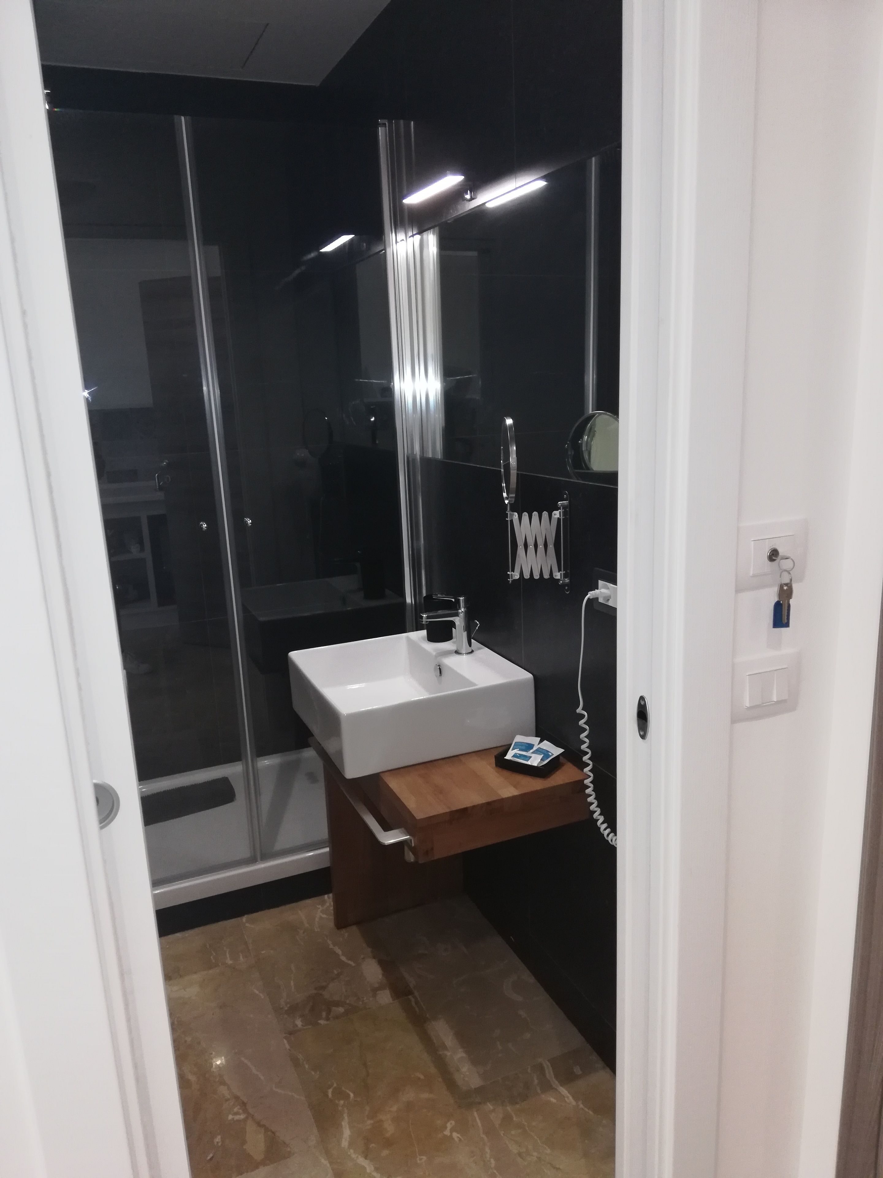 Ein modernes Badezimmer mit einem weißen Waschbecken, einem hölzernen Waschtisch, einer Duschkabine aus Glas und einer weißen Tür.