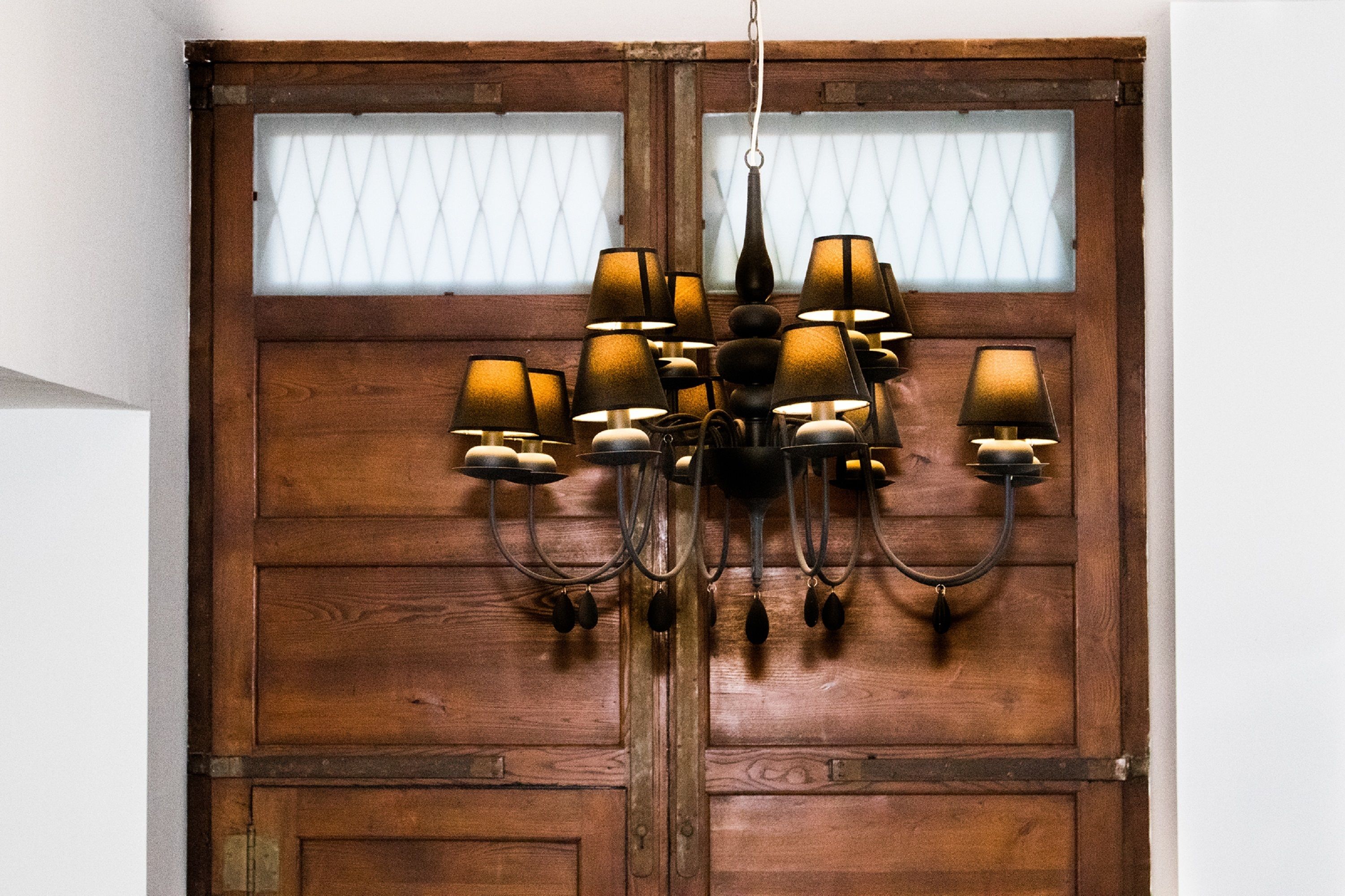 A chandelier with multiple lampshades hanging from a wooden door with glass panels.