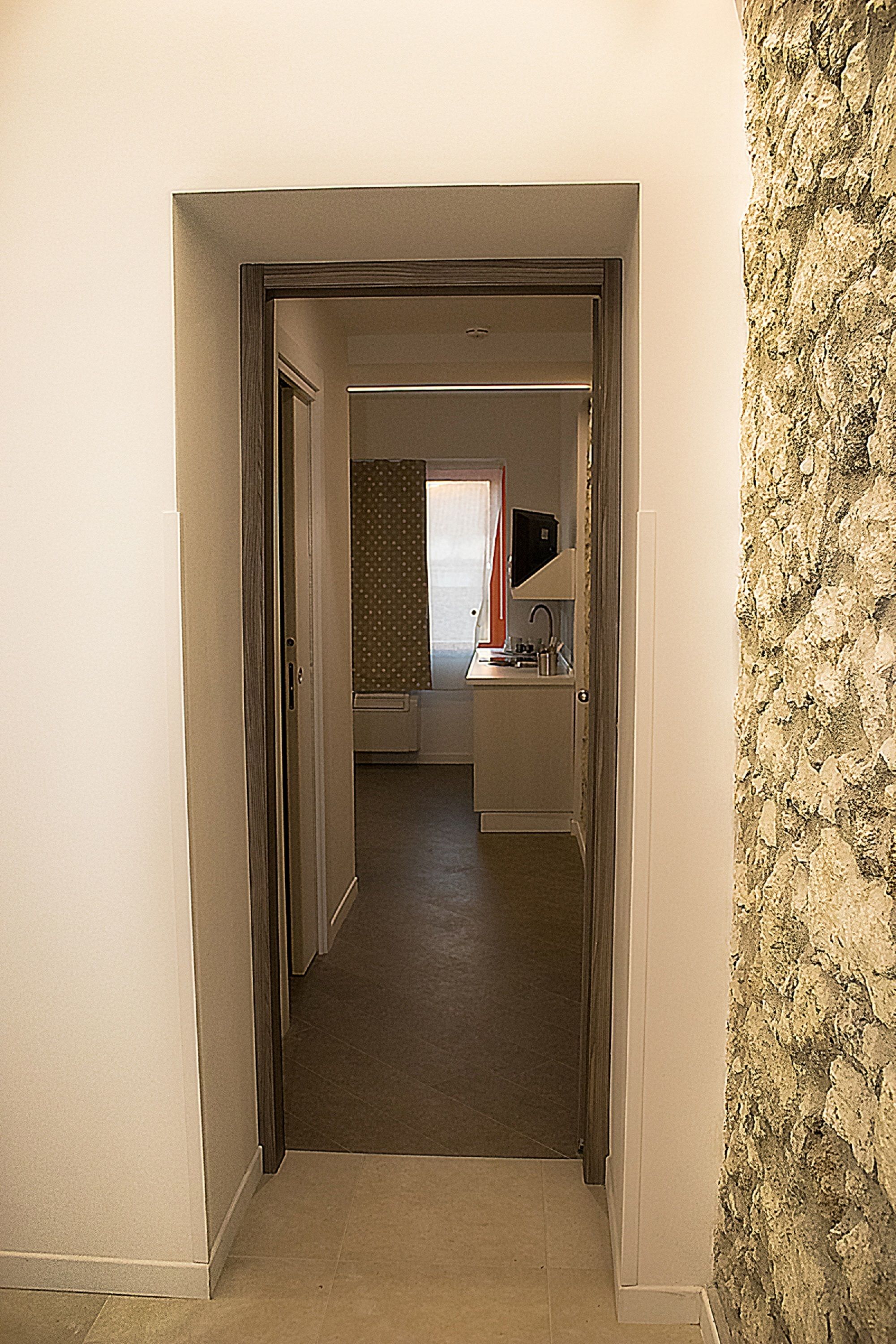 A hallway leading to a room with a kitchenette, a bathroom with a shower curtain, and a stone wall.