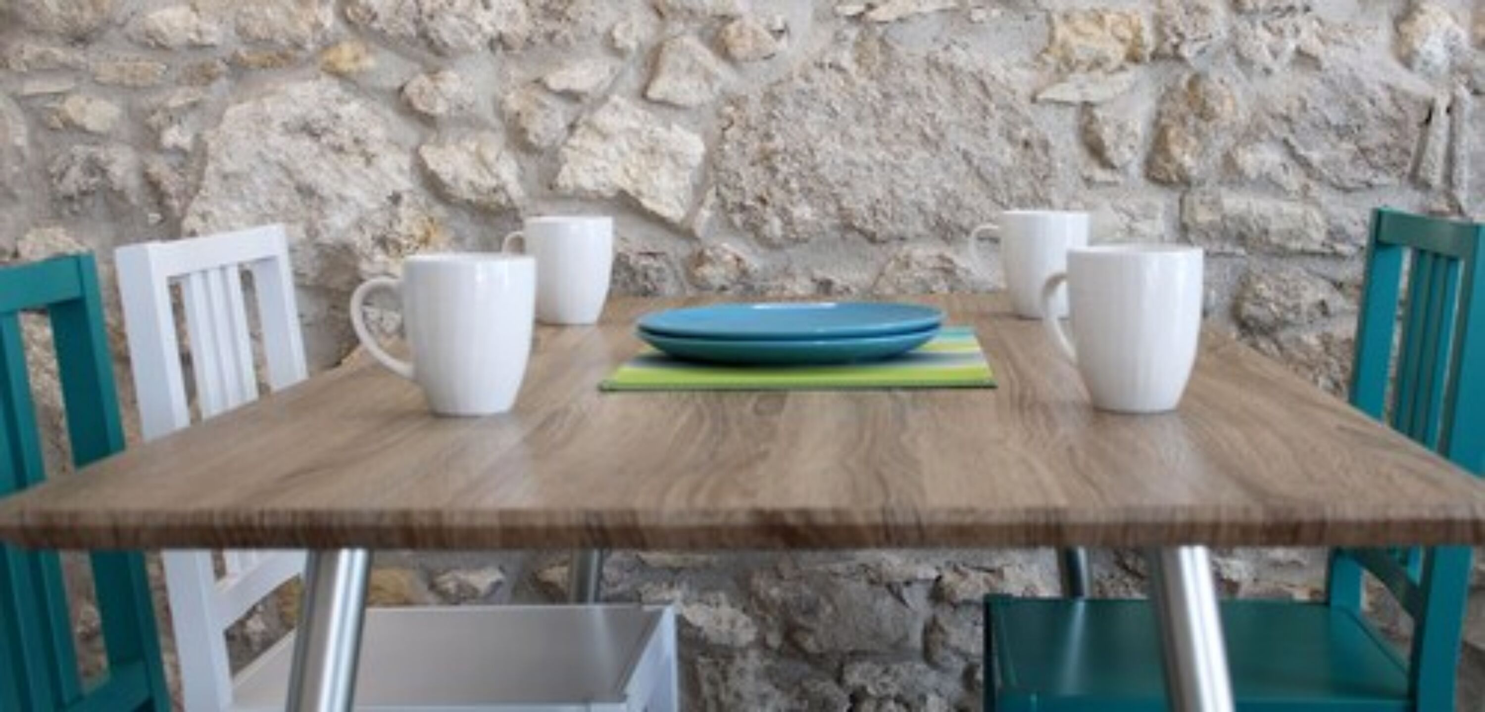 Uma mesa de madeira com cadeiras brancas e azuis, canecas brancas e um prato azul.