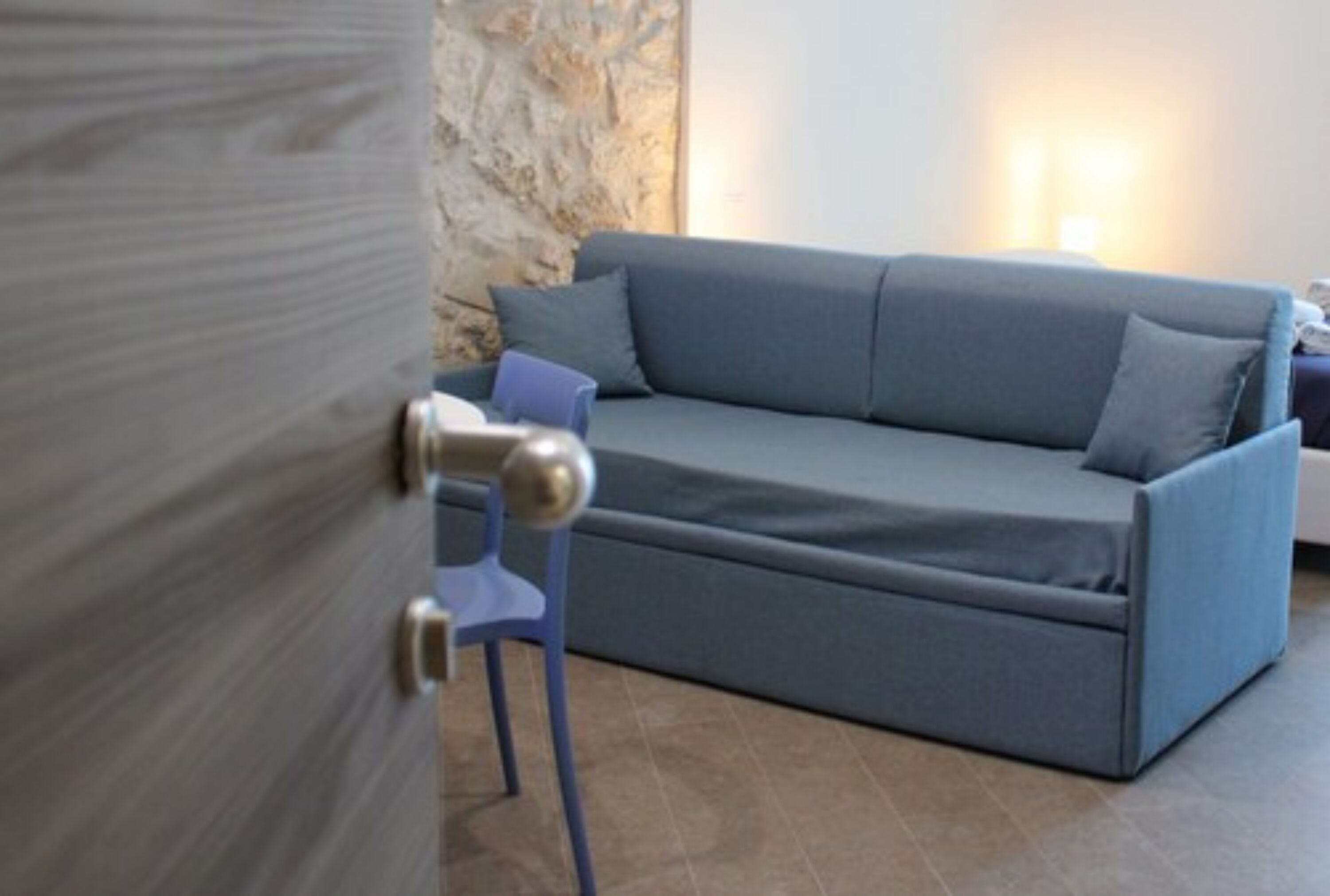 Una habitación con un sofá gris, un sillón azul y una pared de piedra.