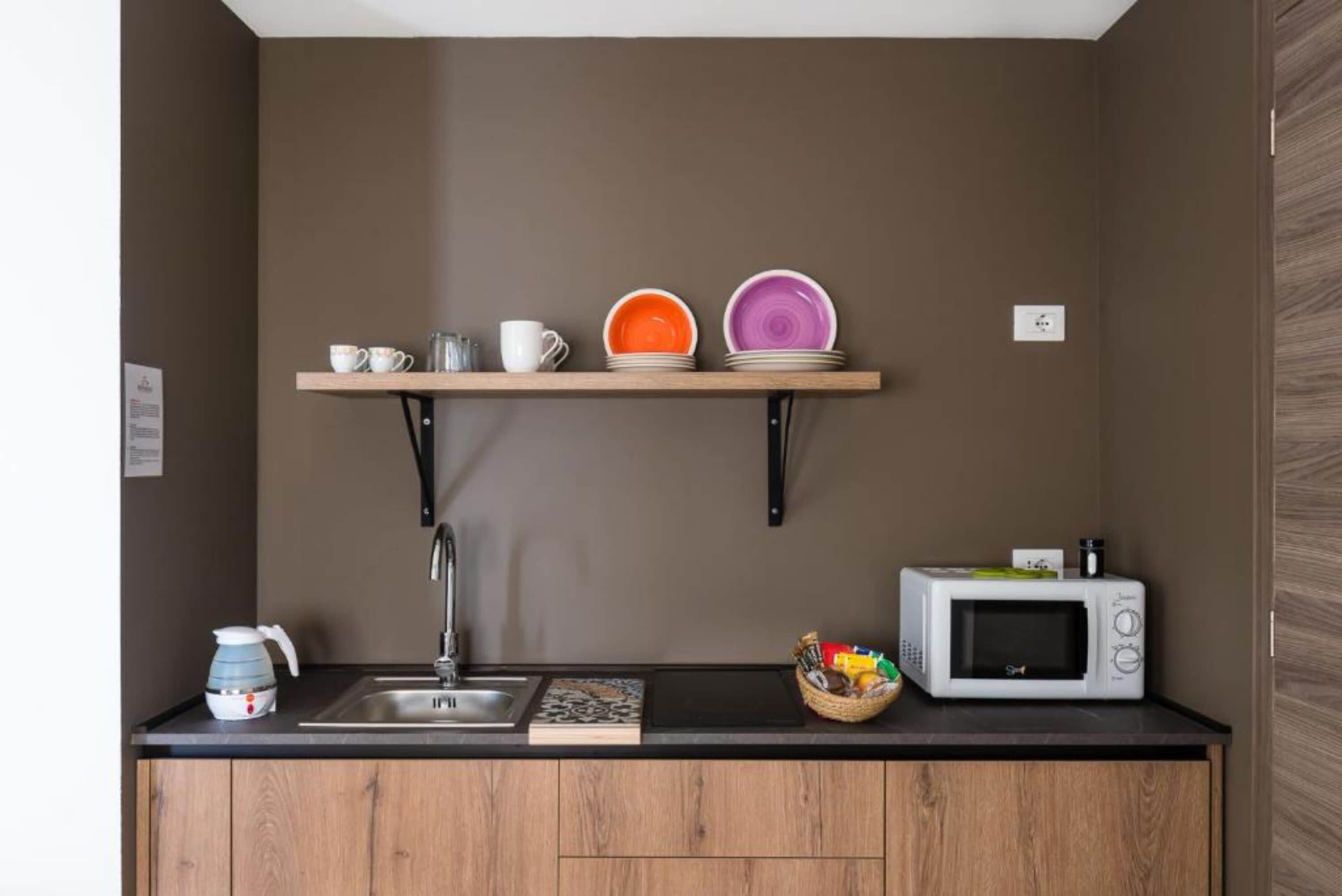 A compact kitchenette with a built-in microwave, a kettle, and a shelf holding dishes.